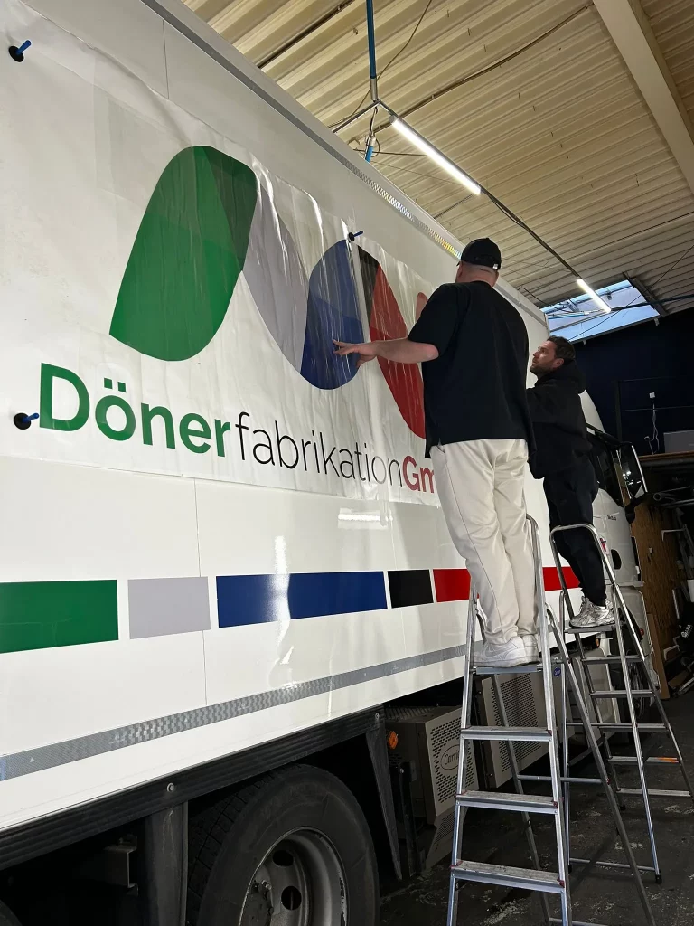 Mitarbeiter von GoMedia bringen eine Dönerwerbung an einem Fahrzeug an.